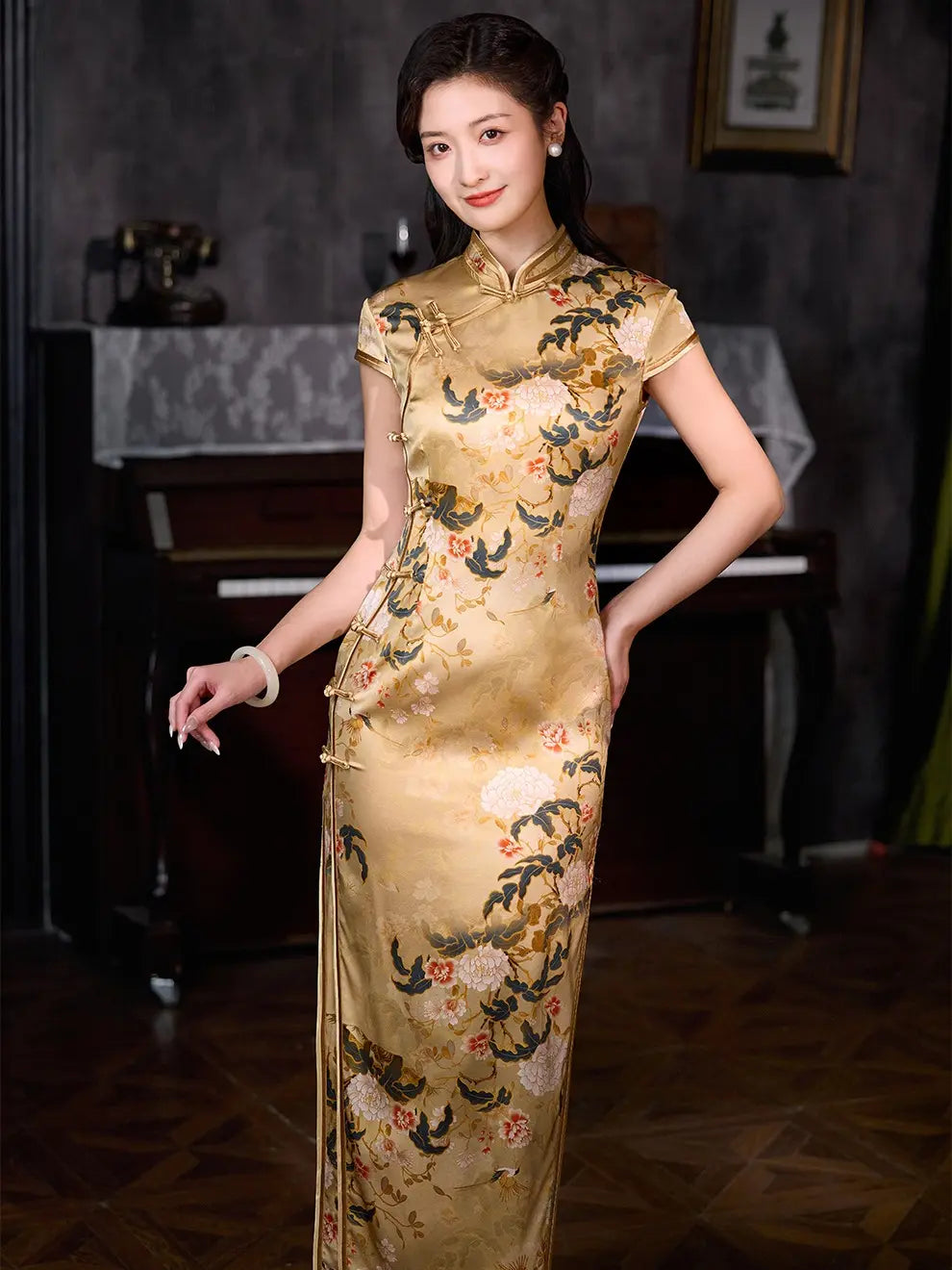 A woman wearing a Vintage Gold Peony Silk Long Qipao cheongsam dress with a floral and bird pattern, standing in a vintage room with a piano in the background.