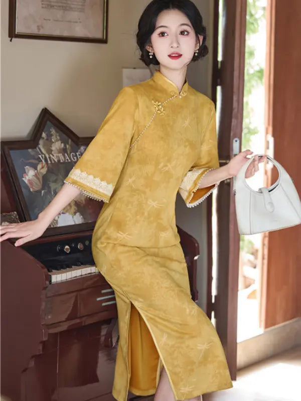 A woman models a yellow cheongsam dress with wide sleeves and a high slit, holding a white handbag in an indoor setting with a piano and doorway.