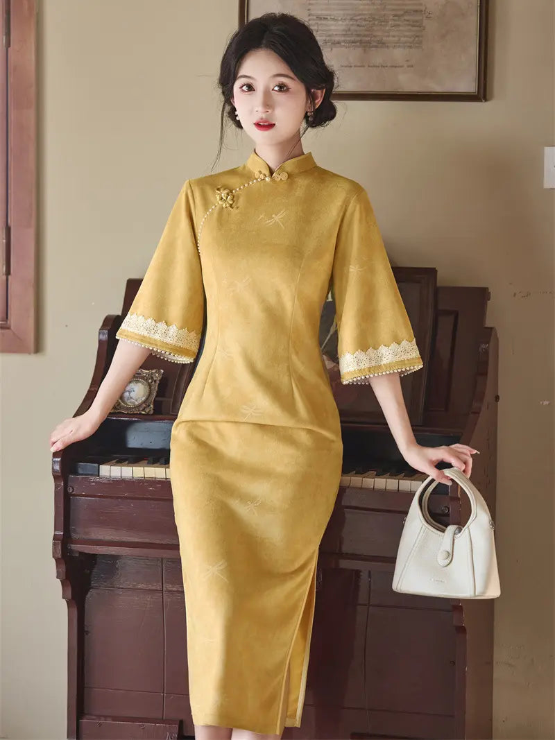 A woman wearing a mustard yellow Chinese cheongsam dress with lace trim on the sleeves, posing in front of a vintage brown piano and holding a white handbag.