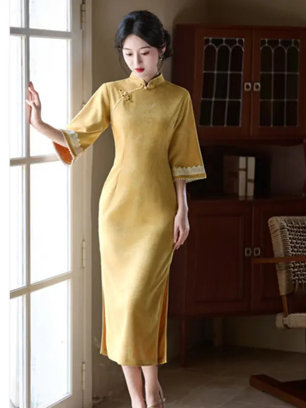 A woman wearing a yellow Chinese cheongsam dress stands by a window in an indoor setting with wooden cabinets in the background.