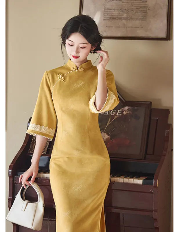 A woman wearing a yellow traditional Chinese cheongsam dress with lace trim on the cuffs and collar, holding a small cream-colored handbag next to a vintage piano.