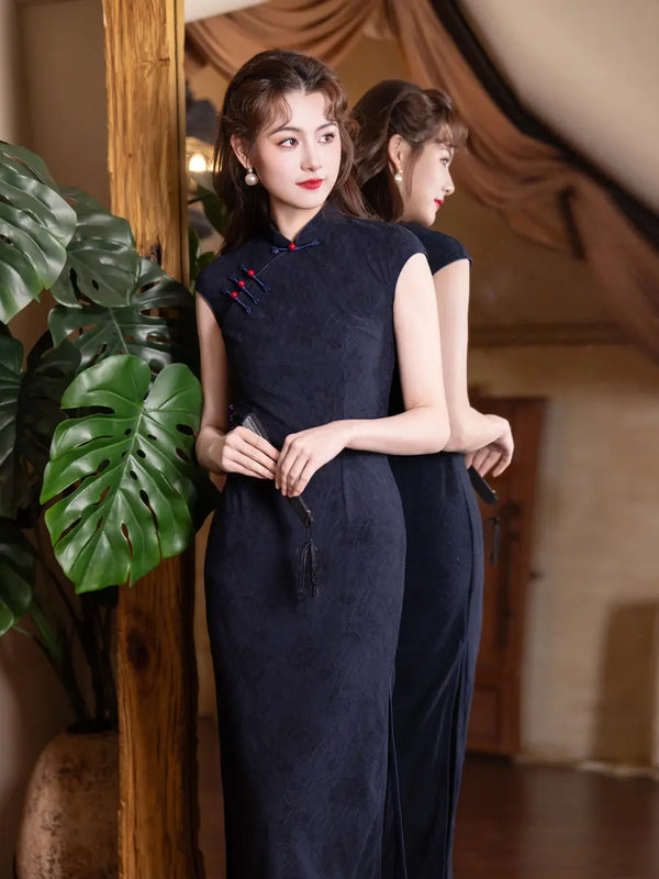 Woman in a long dark Vintage Navy Blue Jacquard  Sleeveless Qipao Dress With Red Buttons standing next to a plant indoors.