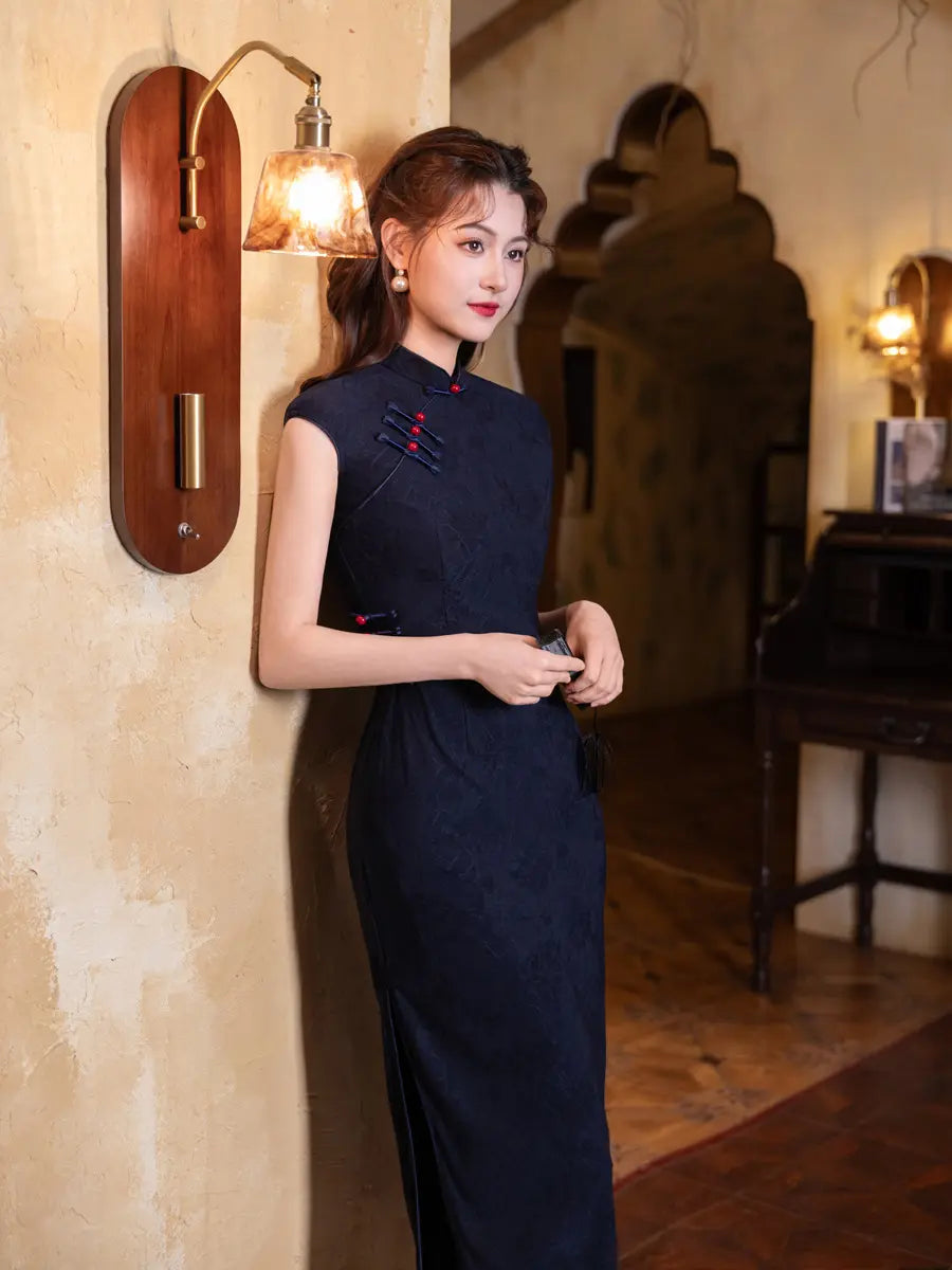 Woman in a dark Vintage Navy Blue Jacquard  Sleeveless chinese cheongsam  Dress With Red Buttons  standing against a wall with warm lighting.