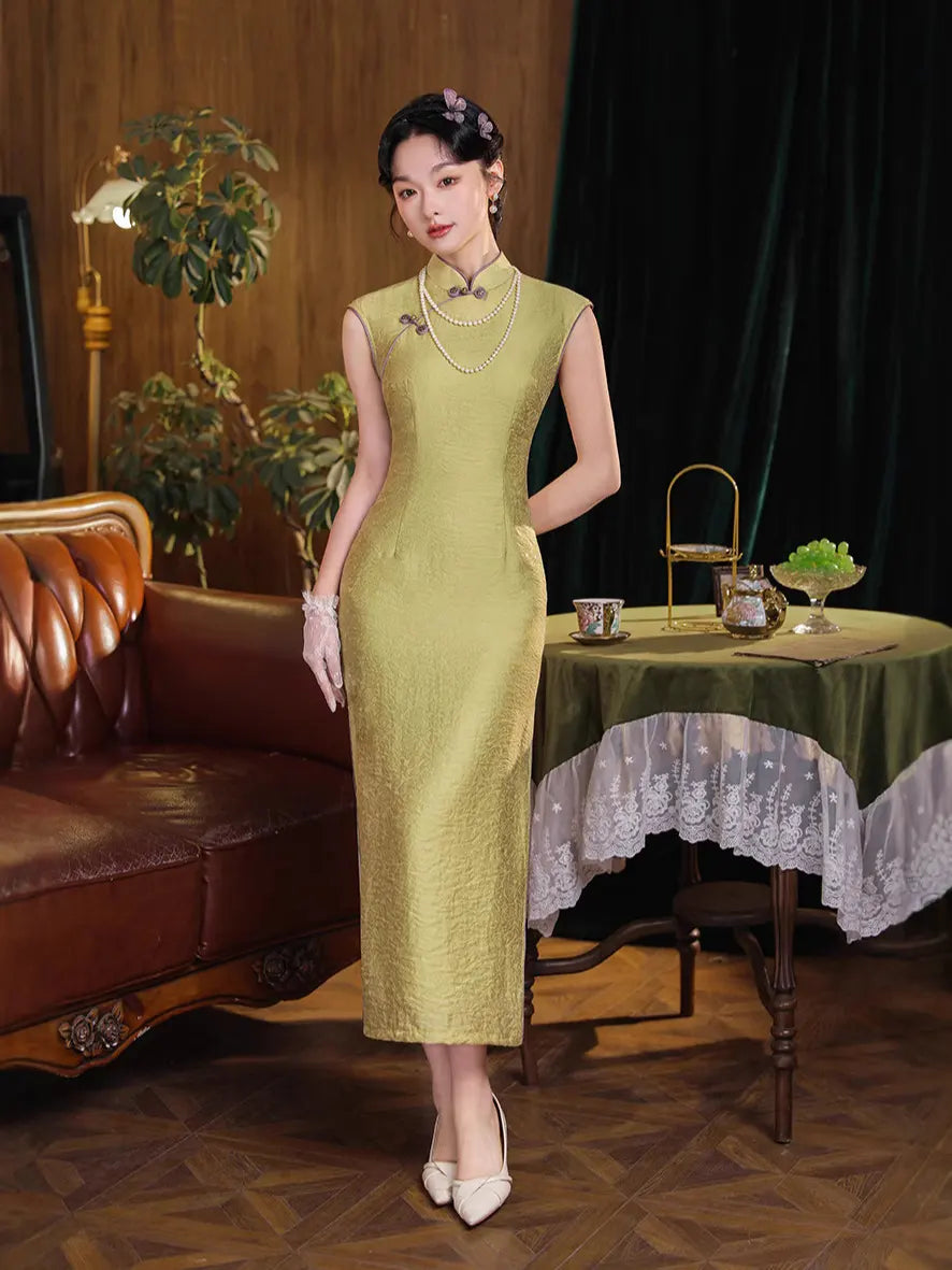 Woman in aVintage Olive Green Long Sleeveless Qipao cheongsam dress standing in a room with a table and plants.