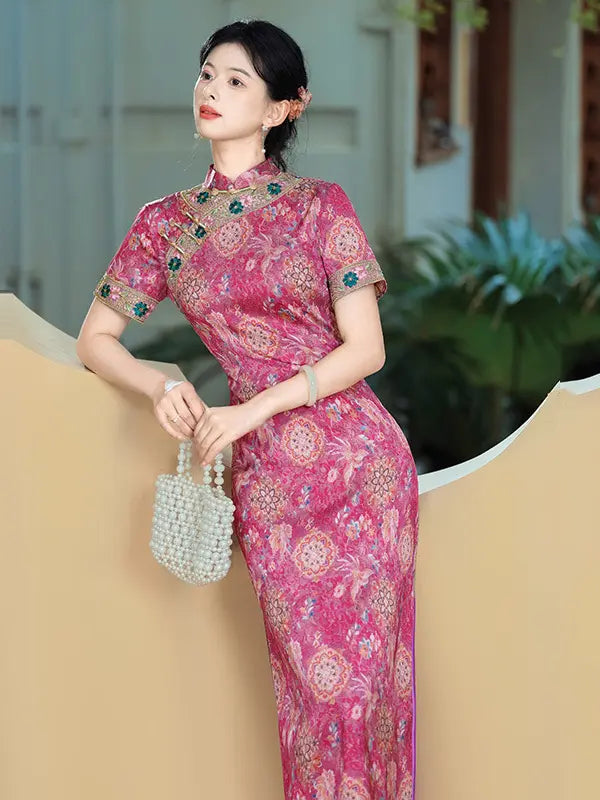 A woman wearing a pink floral-patterned Chinese cheongsam (qipao) dress with short sleeves and a high collar, holding a pearl beaded handbag in an outdoor courtyard setting.