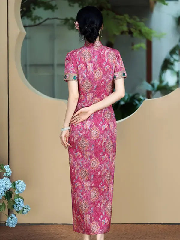 A woman viewed from behind wearing a pink short-sleeve cheongsam dress with an intricate floral and circular pattern, standing in front of a beige wall with a decorative circular window.