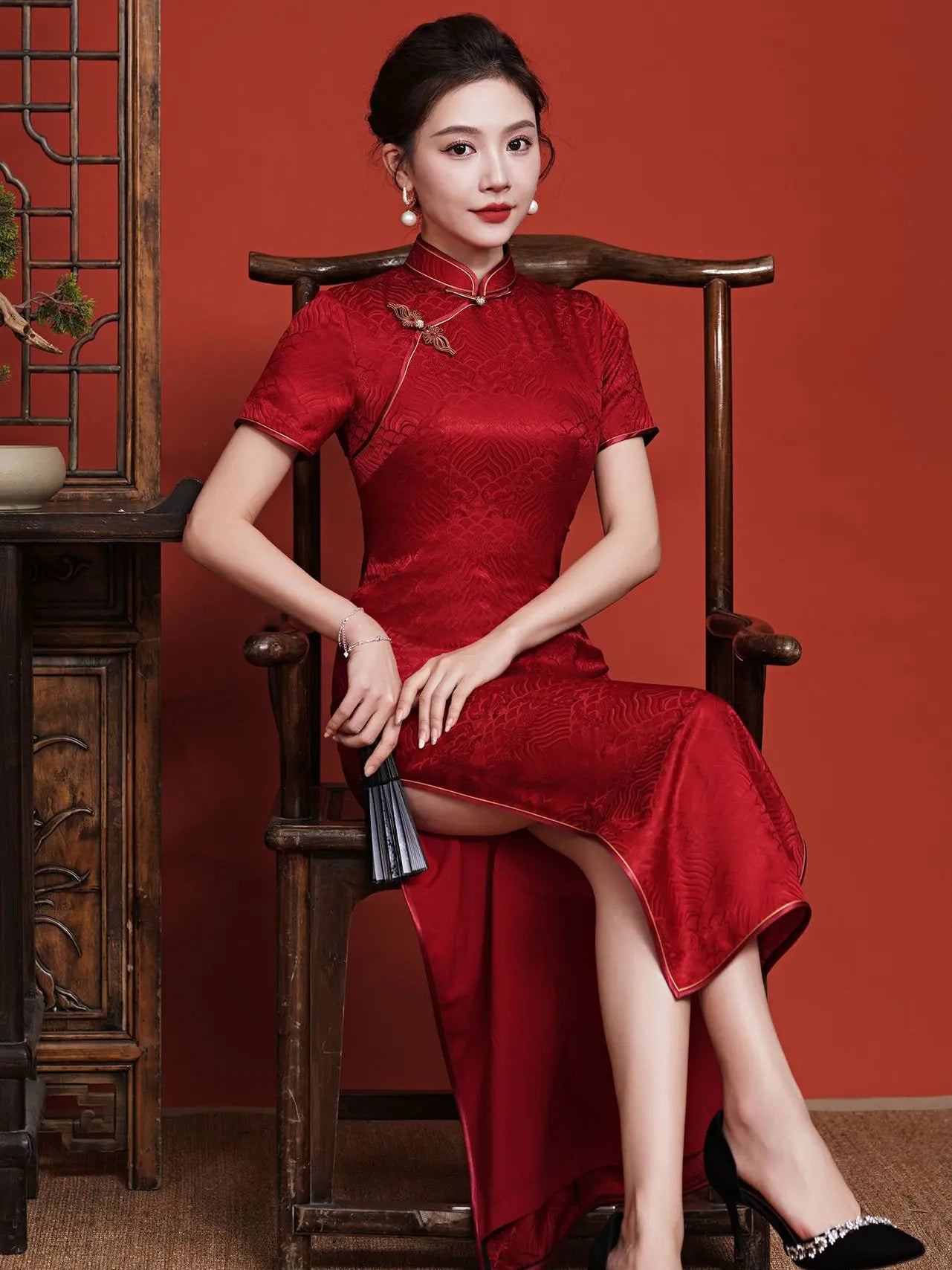 Woman in a Vintage Red  Short Sleeve Mulberry Silk Jacquard Qipao cheongsam dress sitting on a wooden chair against a red background