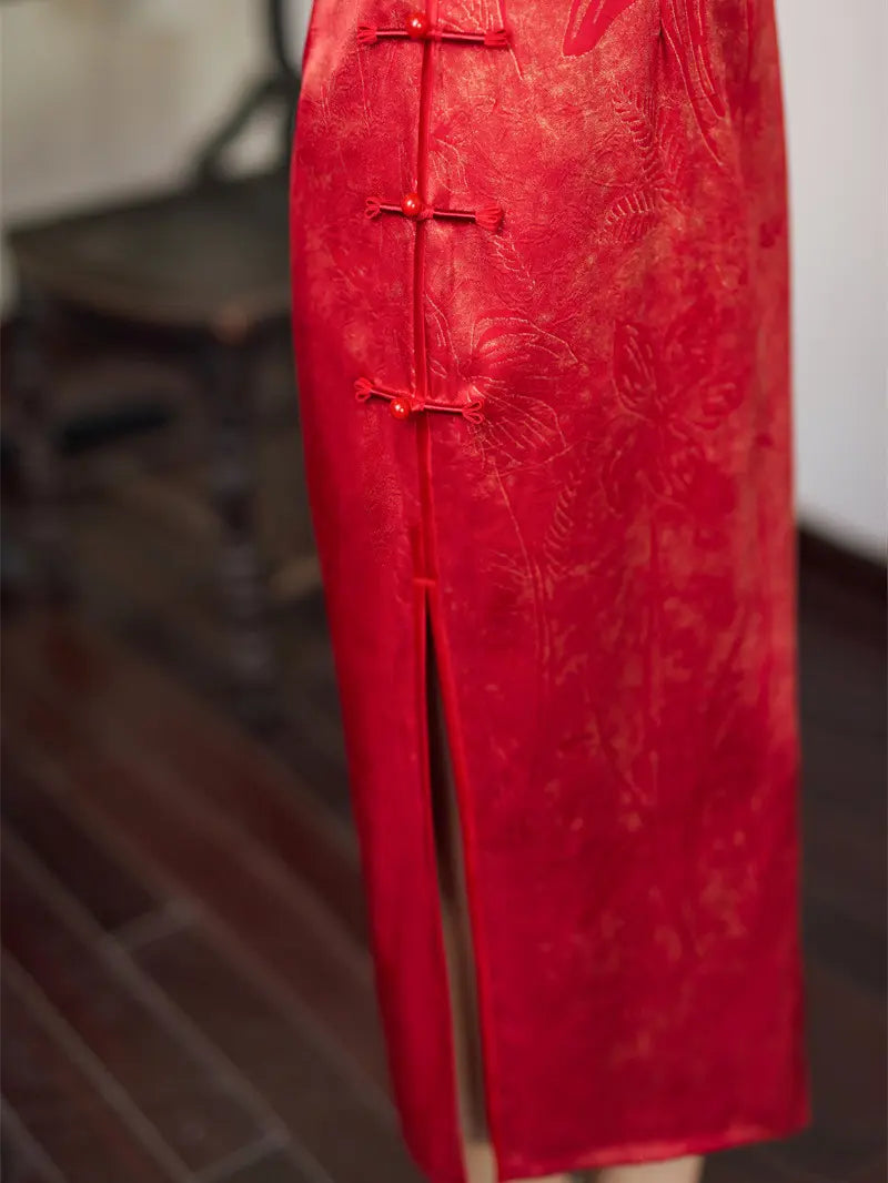 A close-up of a red traditional Chinese cheongsam dress with frog closures and a side slit, shown against a blurred indoor background.