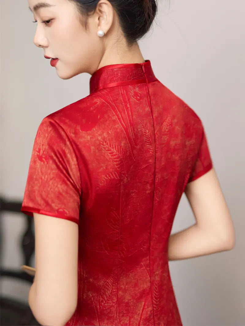 A woman shown from the back wearing a red short-sleeve cheongsam-style dress with a high mandarin collar and subtle tonal floral jacquard pattern.