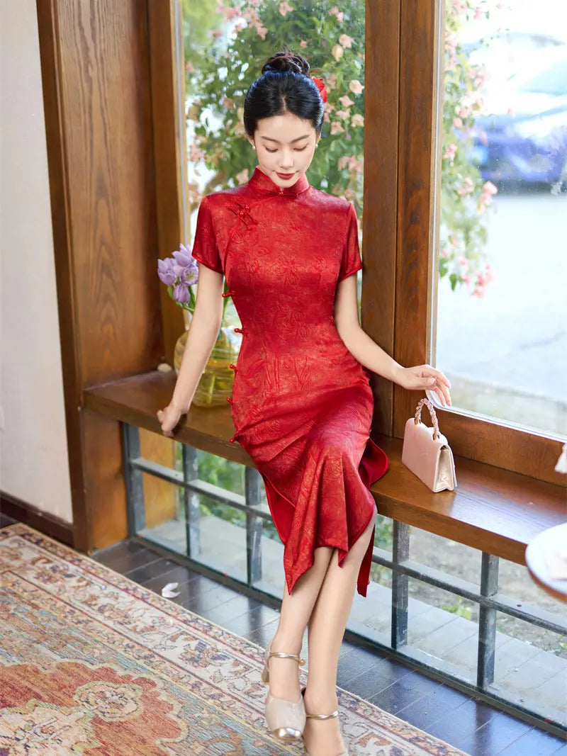 A woman wearing a red short-sleeve cheongsam dress with a subtle floral jacquard pattern, sitting on a wooden window ledge in a cafe setting.