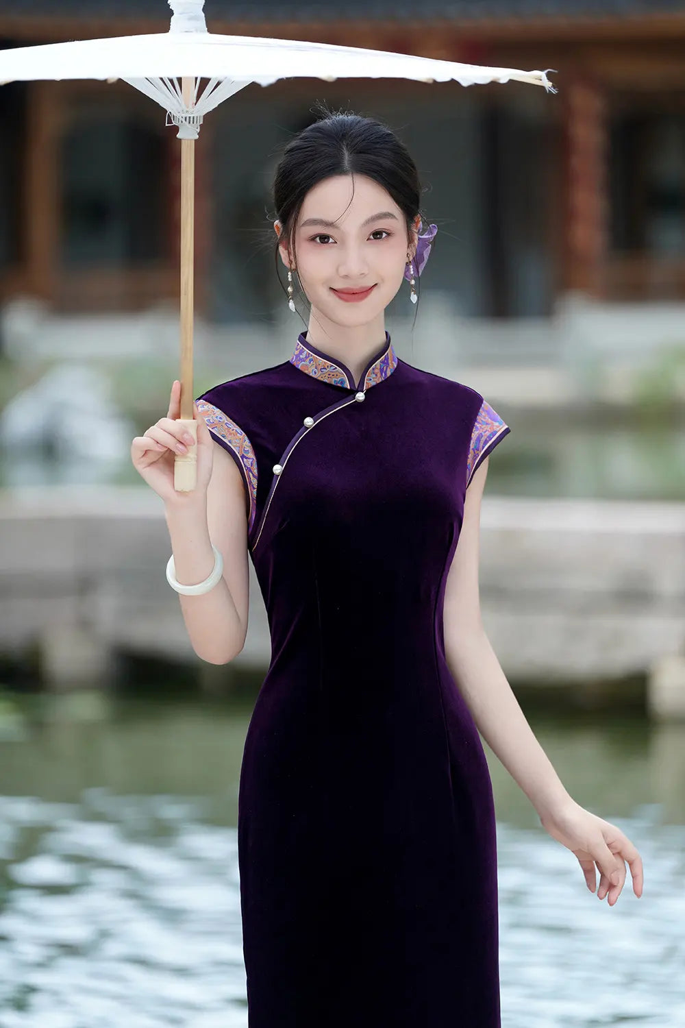 Woman in aViolet Velvet Qipao Cheongsam Dress with Floral Trim  holding an umbrella by a body of water