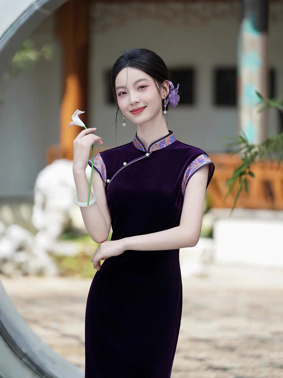 Woman in a traditional Violet Velvet Qipao Cheongsam Dress with Floral Trim  with floral accents standing outdoors.