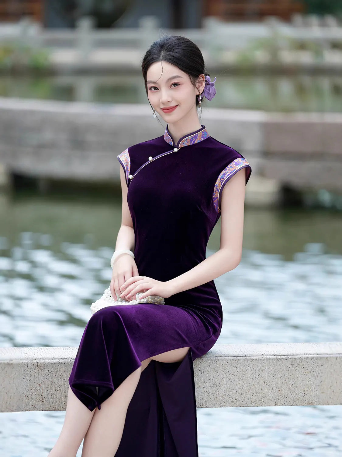Woman in a Violet Velvet Qipao Cheongsam Dress with Floral Trim sitting by a water body