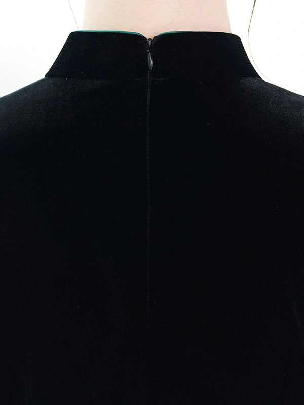 Close-up back view of a black velvet garment on a mannequin, showing a high collar and center zipper.
