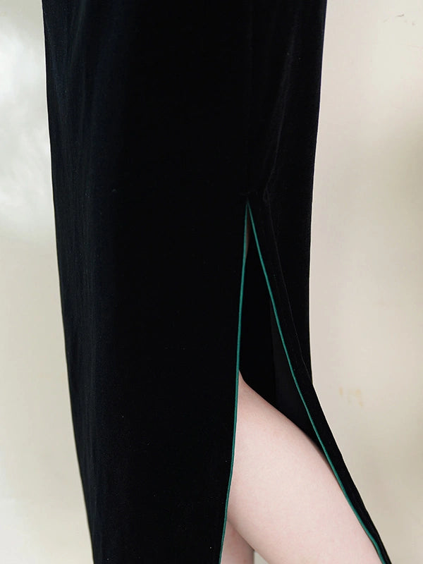 Close-up of a black velvet dress with a high side slit, showing a thin dark green piping accent along the edge and a model's leg visible inside the slit.