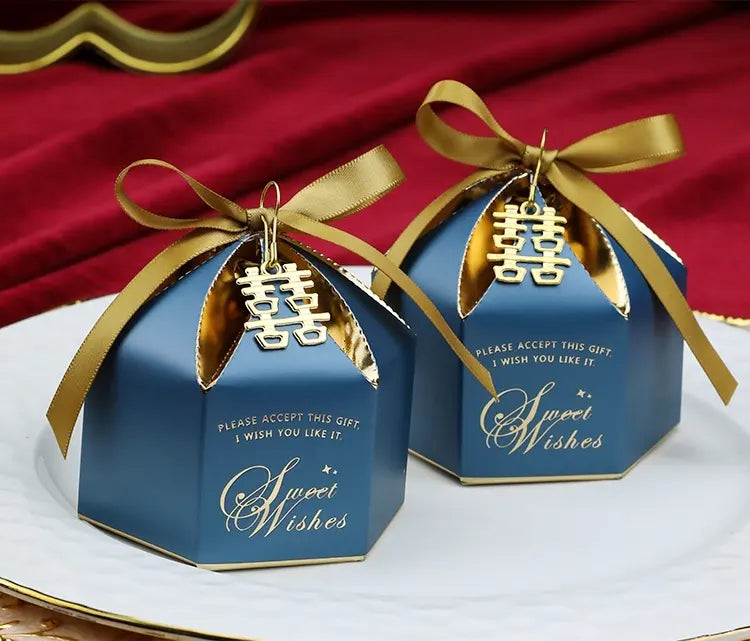 Two blue Wedding Favor Boxes with Double Happiness Charms with gold ribbons and 'Sweet Wishes' text on a red fabric background.