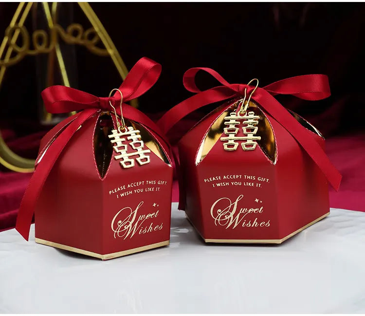 Two red Wedding Favor Boxes with Double Happiness Charm with gold ribbons and 'Sweet Wishes' text on a white surface.