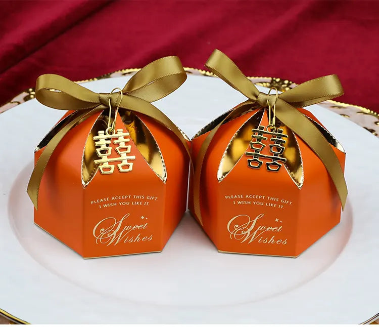 Two orange Wedding Favor Boxes with Double Happiness Charm with gold ribbons and 'Sweet Wishes' text on a white plate with red background.