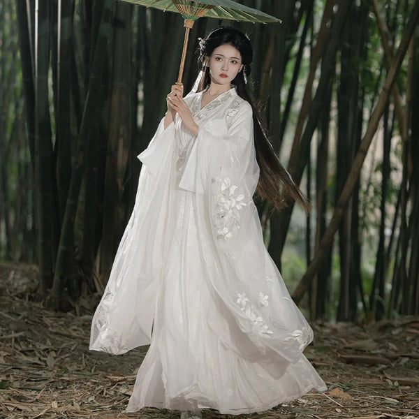 Woman in a traditional White Flowing Chinese Song Dynasty Hanfu Dress dress holding an umbrella in a forest setting