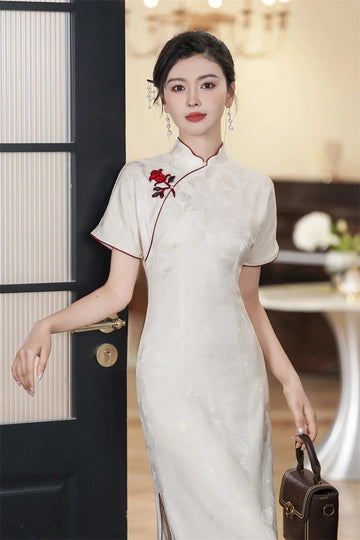 Woman in a white traditional Jacquard Qipao Cheongsam Dress With Red Trimwith red floral embroidery, holding a brown handbag indoors.