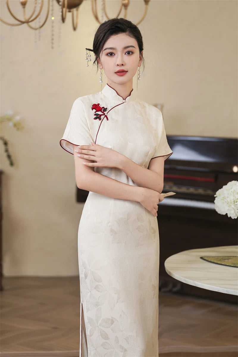 Woman in a white traditional Jacquard Qipao Cheongsam Dress With Red Trim with a red flower in an elegant indoor setting