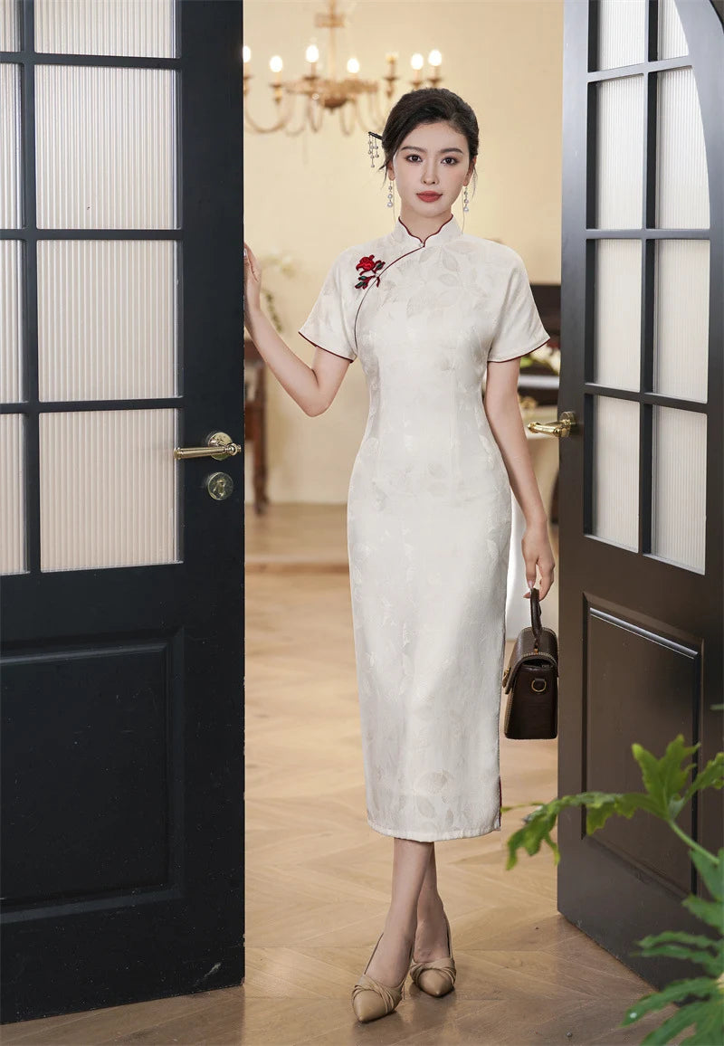 Woman in a White Jacquard Qipao Cheongsam Dress With Red Trim  standing in a doorway with a plant in the foreground