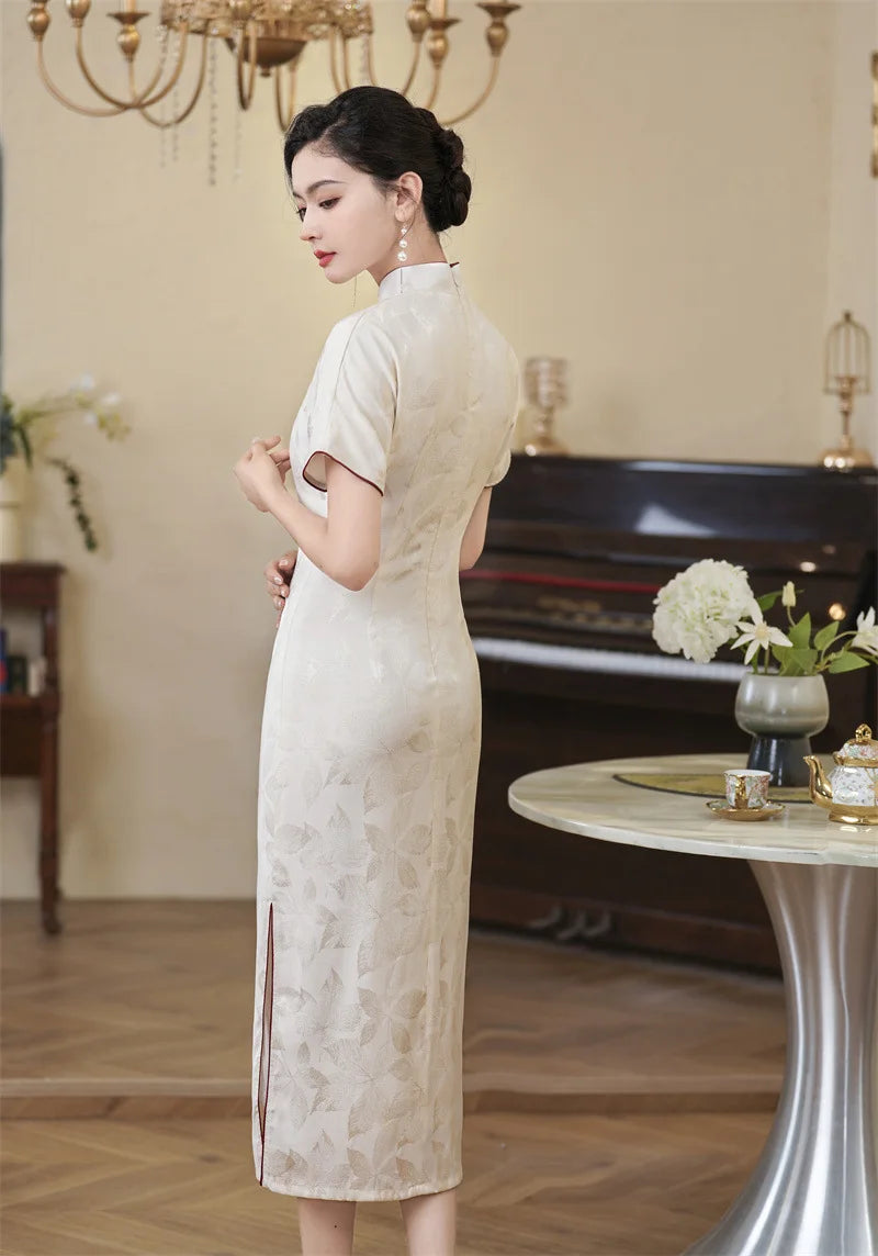 Woman in a long, light-colored White Jacquard Qipao Cheongsam Dress With Red Trim standing in an elegant room with a chandelier and table.