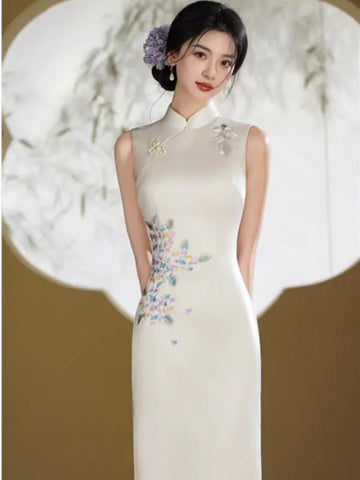 A woman wearing a sleeveless cream-colored Chinese cheongsam dress with floral embroidery on the side, standing against a decorative circular backdrop.