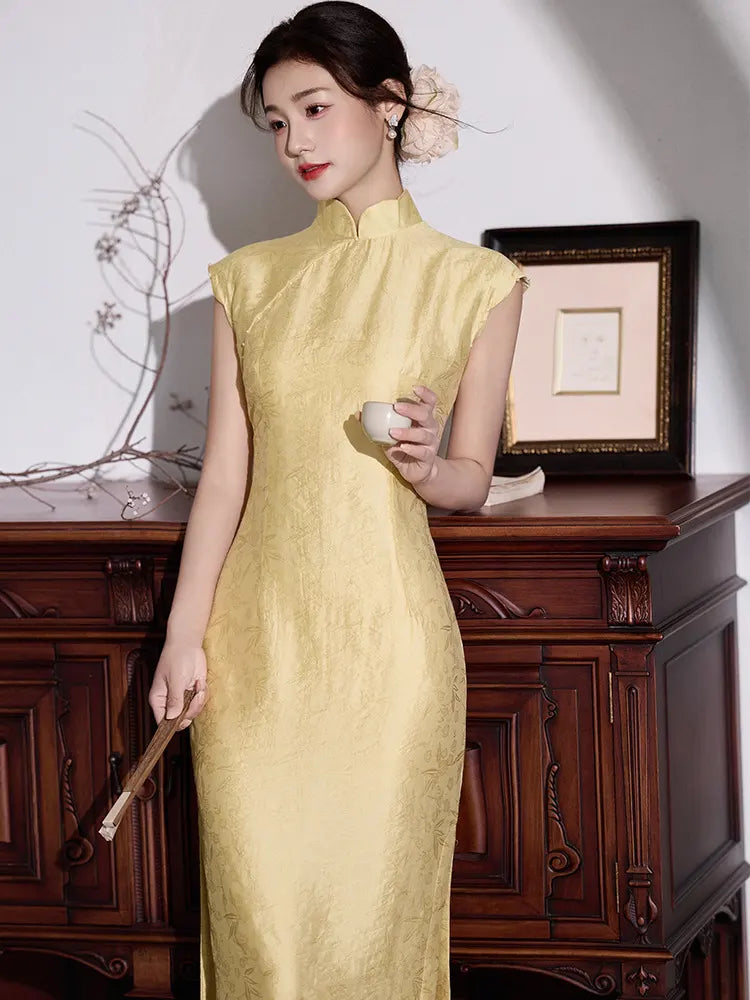 Woman in a yellow traditional  Floral Sleeveless Midi Cheongsam Qipao Dressholding a small white cup in a room with wooden furniture.