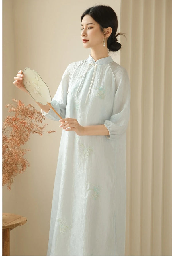 A Chinese Woman in aZen-Inspired Light Blue Loose Cheongsam Qipao Dressholding a dried flower arrangement against a beige background