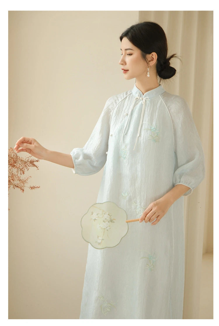 a chinese Woman in a Zen-Inspired Light Blue Loose Cheongsam Qipao Dress holding a fan against a neutral background