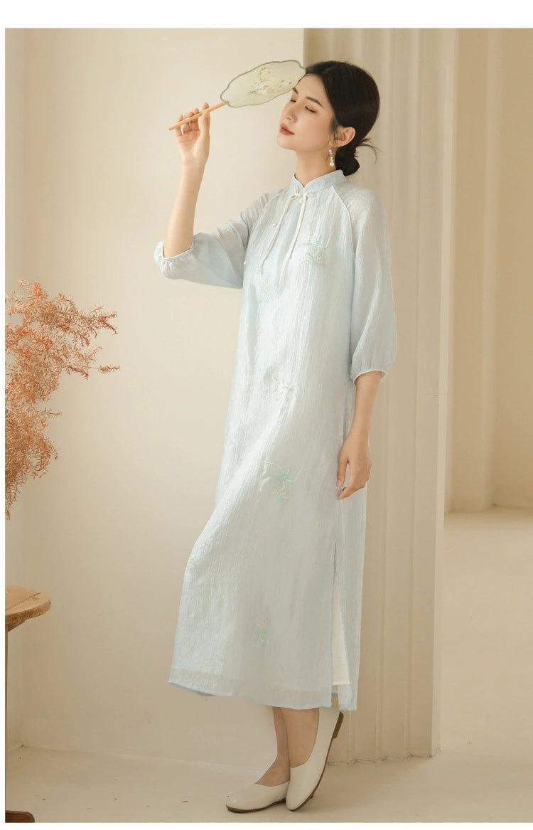 a chinese Woman in a Zen-Inspired Light Blue Loose Cheongsam Qipao Dress holding a fan in a softly lit room.