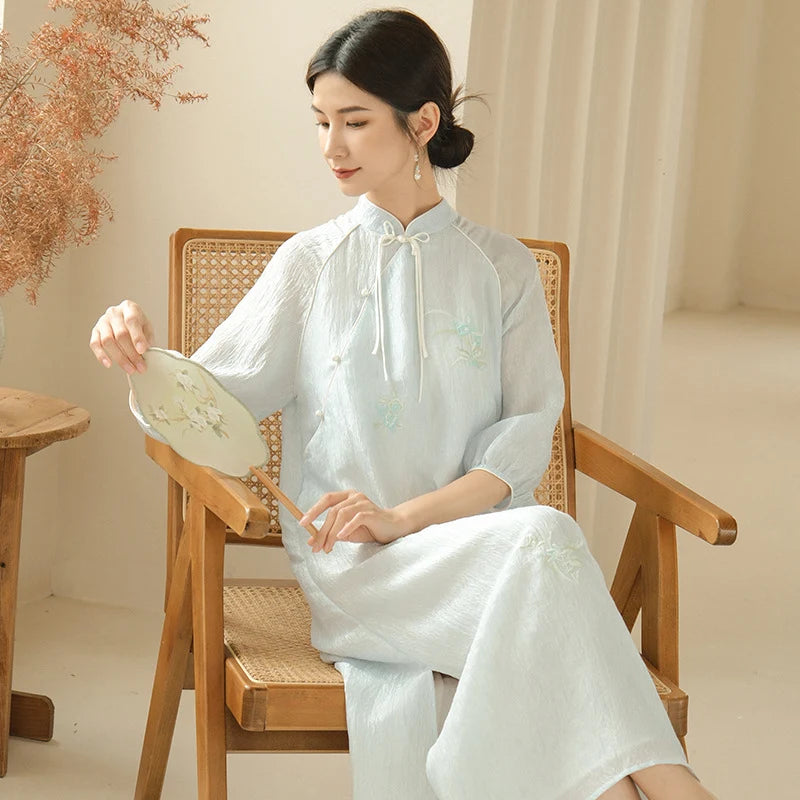 a chinese girl in a Zen-Inspired Light Blue Loose Cheongsam Qipao outfit sitting on a wooden chair holding a round object.