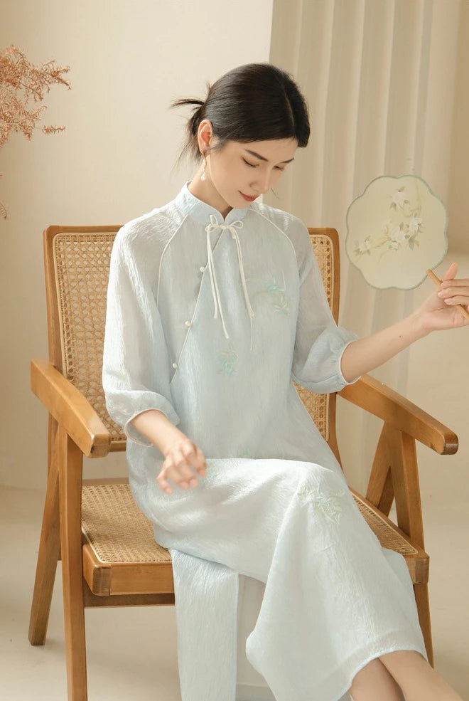 a chinese Woman in a Zen-Inspired Light Blue Loose Cheongsam Qipao Dress outfit sitting on a wooden chair.