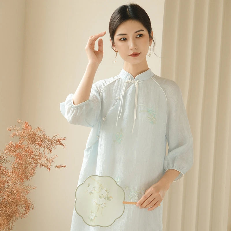 a chinese Woman wearing a Zen-Inspired Light Blue Loose Cheongsam Qipao Dress holding a fan indoors.