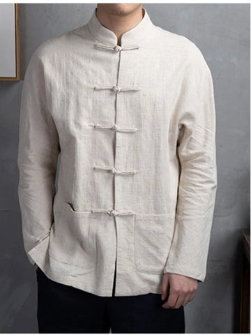 A man wearing a light beige linen long-sleeve jacket with traditional Chinese frog closures, paired with dark pants, standing against a textured gray wall.