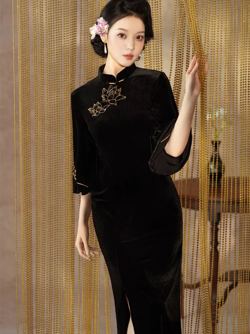 A woman models a black velvet cheongsam-style dress with gold floral embroidery on the chest, posed in front of a gold beaded curtain backdrop.