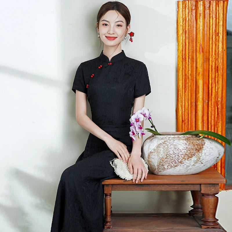 Woman in a black  Short Sleeve Floral A Line Qipao cheongsam outfit sitting on a wooden bench with a decorative vase and flowers.