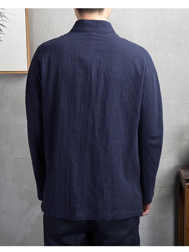 A man viewed from the back wearing a dark navy blue, long-sleeve linen chinese tang shirt with a high collar, set against a textured gray wall.