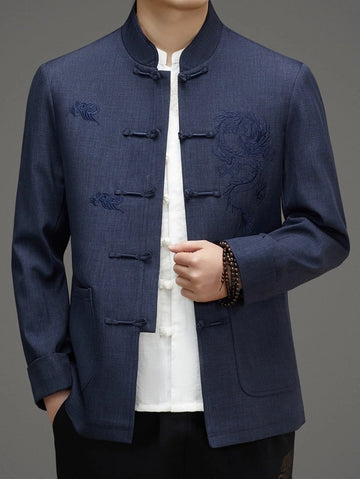 A man wearing a navy blue traditional Chinese jacket with dragon embroidery on the chest, paired with a white shirt and black pants, shown against a neutral gray background.