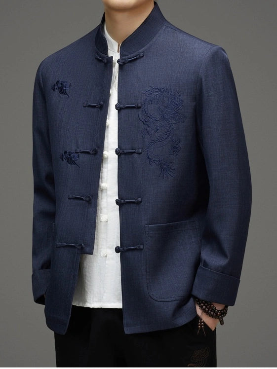 A man wearing a navy blue traditional Chinese-style jacket with dragon embroidery on the chest, paired with a white shirt and black pants, shown from the neck down against a neutral gray background.