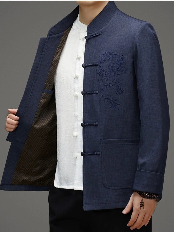 A man wearing a navy blue traditional Chinese-style jacket with frog closures over a white button-up shirt, shown against a plain gray studio background.