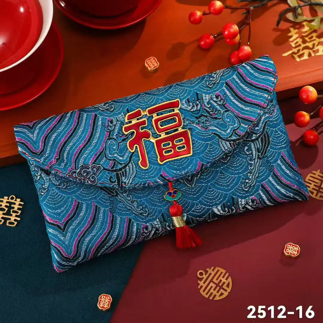A blue embroidered red envelope hongbao with a red tassel and a large red Chinese character on the front, styled on a wooden surface with red cups, decorative ornaments, and gold motifs.