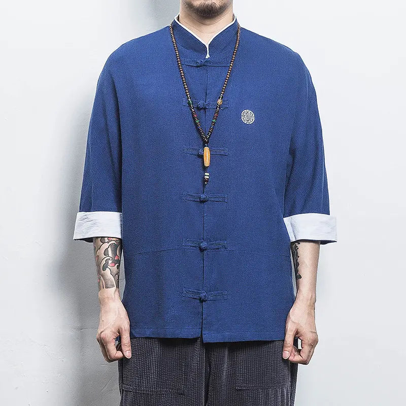 Person wearing a blue traditional  Three-Quarter Sleeve Zen Heritage Linen-Blend Kong Fu Tang Shirt jacket with white cuffs and collar against a plain background
