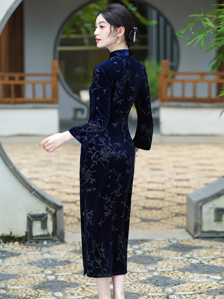A woman wearing a dark navy blue Velvet Long Sleeve Qipao  cheongsam dress with a subtle floral pattern, standing in a traditional courtyard with stone and wood elements.