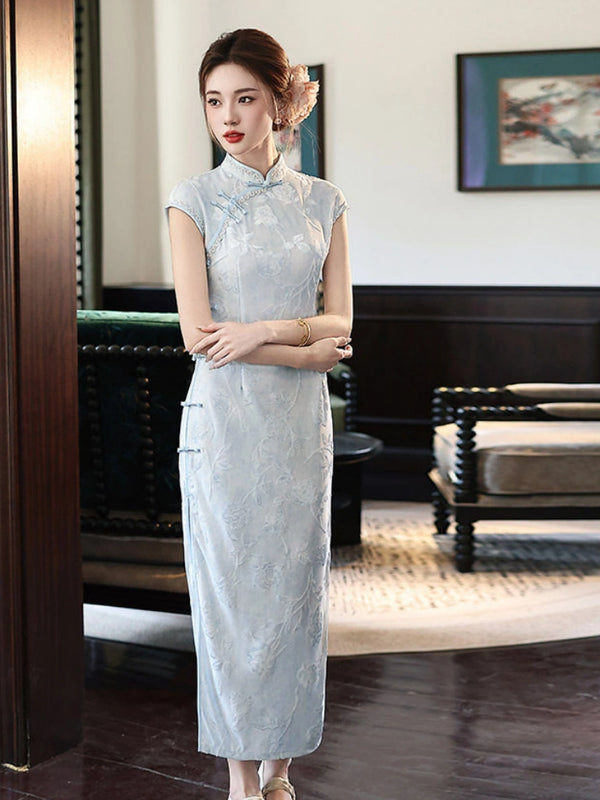 Woman in a light blue traditional Vintage Floral Burnout Velvet Jacquard Qipao cheongsam dress standing in a room with a couch and framed picture.
