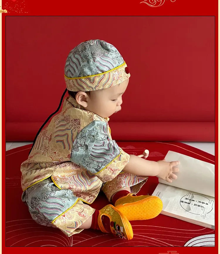Child in traditional Chinese Blue and Gold Baby Tang Jacket Set outfit sitting on a red surface with a book
