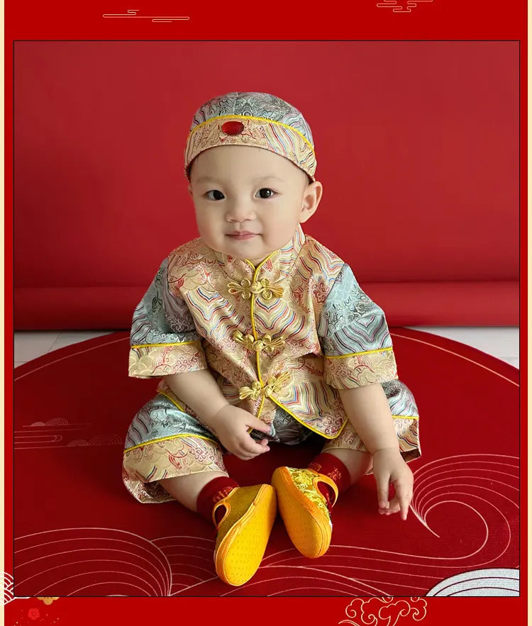 Baby in traditional Chinese Blue and Gold Baby Tang Jacket Set outfit sitting on a red background