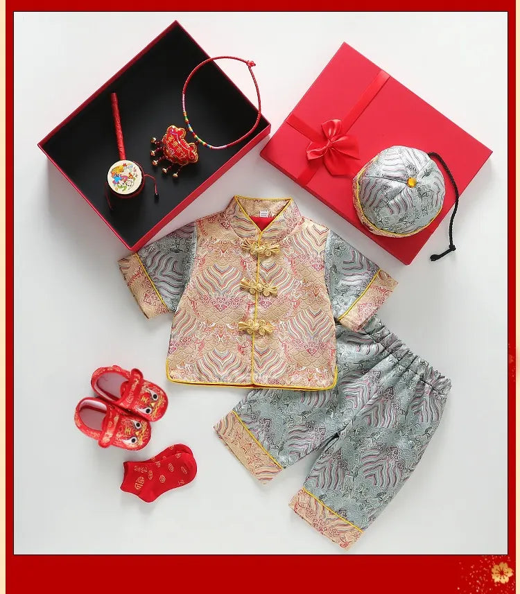 Traditional Chinese baby outfit with red and gold accents, including a top and pants, displayed on a white background.