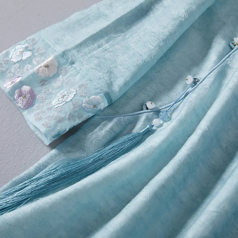 Light blue fabric with floral embroidery and tassels on a gray background
